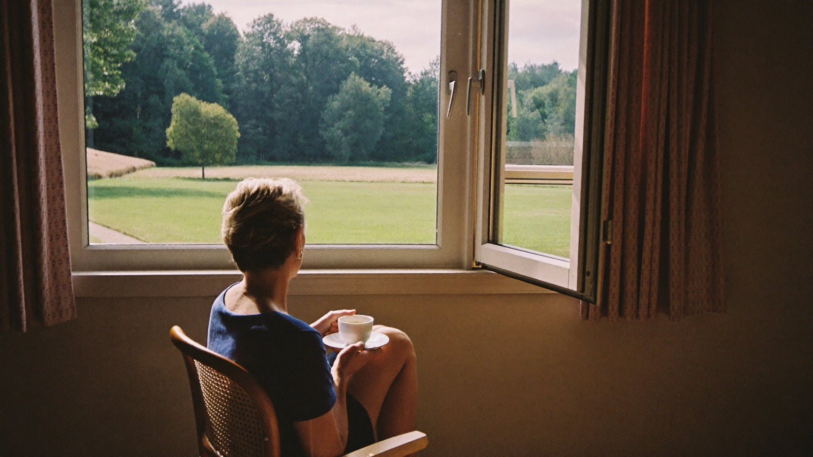A woman at home in soft morning light, looking out the window